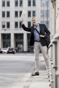 Grey-haired businessman with newspaper calling a taxi in the city