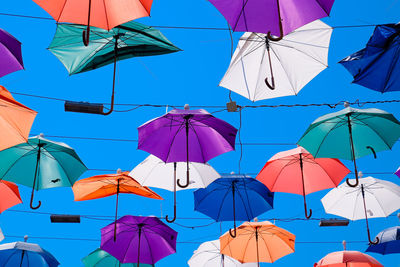 Low angle view of umbrellas hanging against blue sky