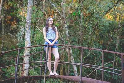 Portrait of young woman standing by railing in forest