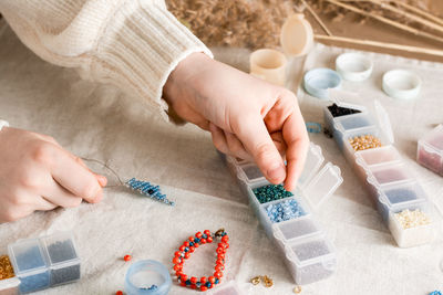 The girl's hands take beads from the box and weave a dolphin. 