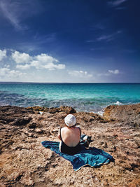 Woman sitting on shore at beach against sky