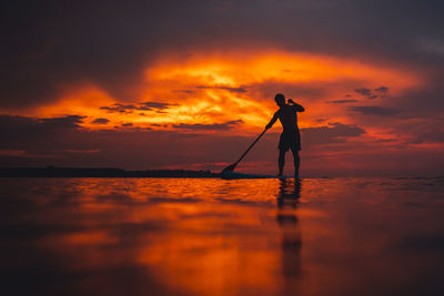 Silhouette man standing in sea against sky during sunset