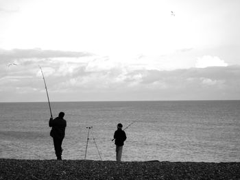 Men fishing in sea against sky