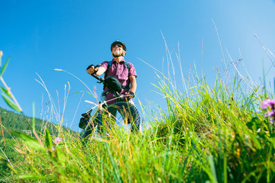 Boy riding bicycle on field against clear blue sky