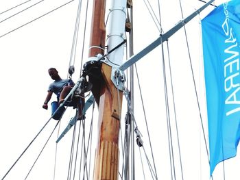 Low angle view of men working on pole against sky