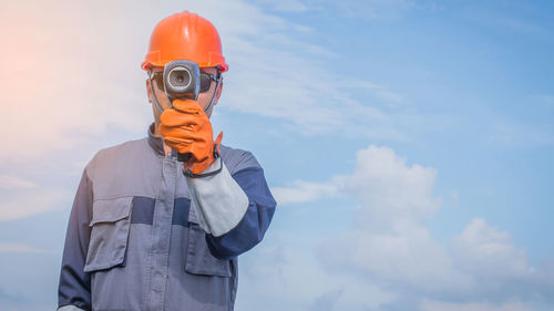 Manual worker holding equipment while standing against sky