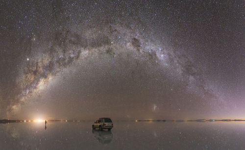 Car over water under the milky way in panoramic view