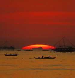 Silhouette people on sailboat in sea against orange sky