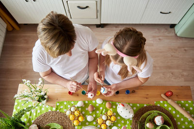 Mom and daughter are preparing for easter and painting eggs with brushes, top view