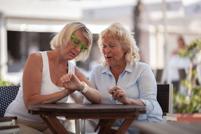 Friends checking time while sitting at sidewalk cafe