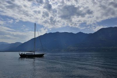 Sailboat sailing on sea by mountains against sky