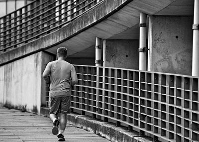 Rear view of man jogging on footpath in city