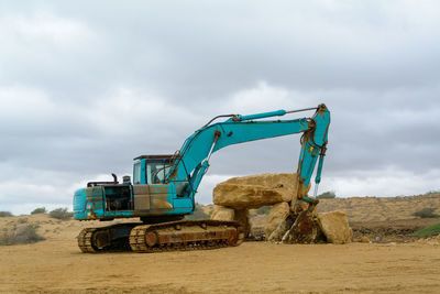 Back side view of industrial rusty blue excavator parked in the beach with cloudy sky