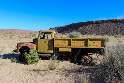 Abandoned truck on field against clear blue sky