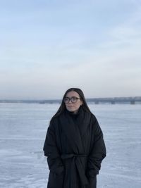 Young woman standing on snow covered sea against sky