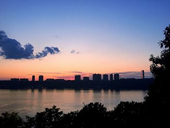 Scenic view of lake by silhouette city against sky during sunset