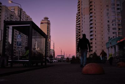 People on road by buildings against sky at dusk