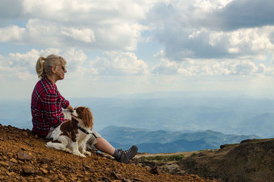 Rear view of woman with dog sitting against sky
