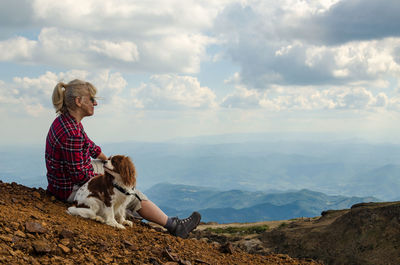 Woman and her dog, cavalier king charles spaniel, are watching picturesque mountain landscape