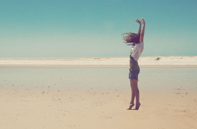 Full length side view of woman standing at beach against sky during sunny day