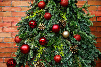 Fir tree decorated with christmas balls over red brick wall