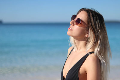 Close up portrait of young woman in black bikini and brown sunglasses on beach in eastern australia