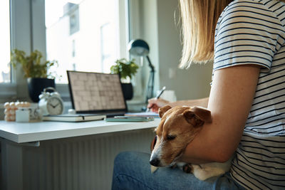 Woman working at home office, use laptop and hold dog on hands