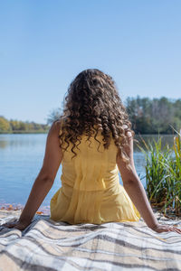Beautiful caucasian woman in yellow dress on a picnic outdoors, sitting next to water