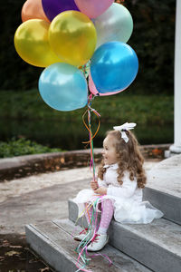 Girl holding helium balloons while sitting on steps