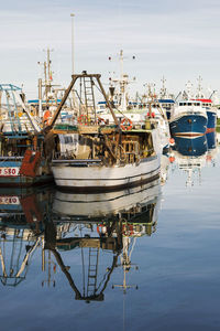 Boats moored at harbor with reflection in sea against sky