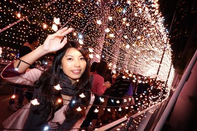 Portrait of smiling woman by illuminated string lights at night