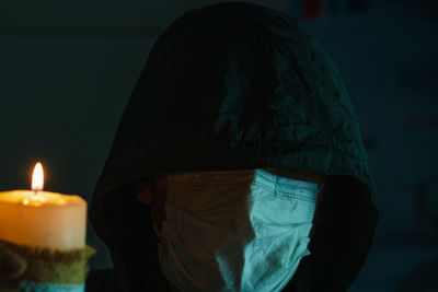 The man's head is concealed by a black hood and a medical mask against the background 