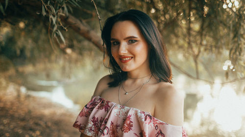 Portrait of young woman standing against trees