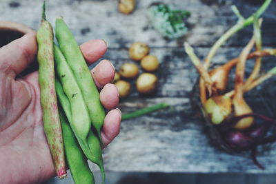 Cropped hand of person holding green beans over wooden table