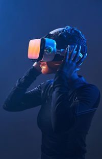 Astonished female african american gamer in modern vr goggles standing on dark background in studio while experiencing virtual reality in neon illumination