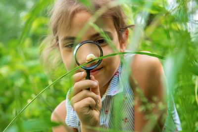 Front view of smiling girl looking at snail on grass through magnifying glass