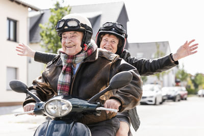 Happy senior couple having fun, riding motor scooter and waving