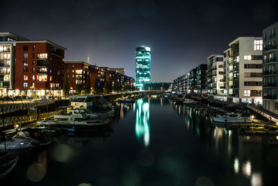 Boats moored in canal against illuminated buildings in city at night