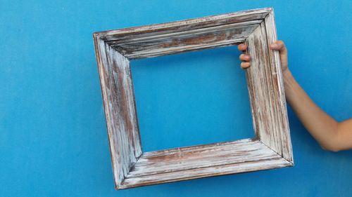 Close-up of hand holding picture frame against blue background