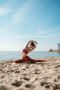 Full length of woman exercising on beach against sky