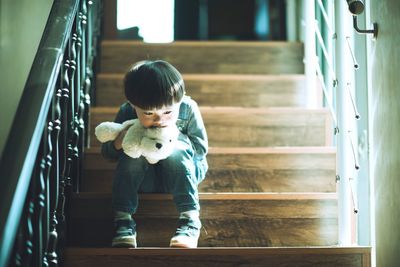 Low angle view of sad boy with stuffed toy sitting on steps at home