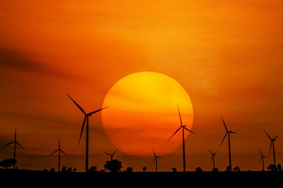 Silhouette wind turbines on field against orange sky