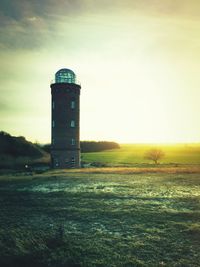 Lighthouse on field against sky at sunset