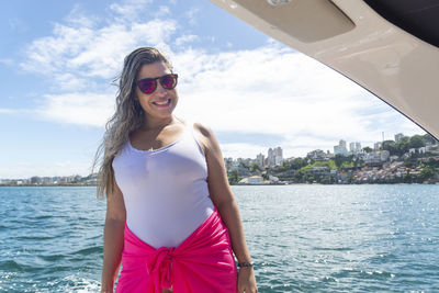 Portrait of young woman wearing sunglasses while standing against sea