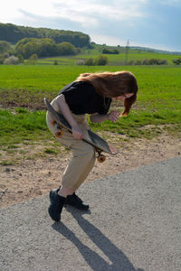 Young girl with a skateboard in her hand, laughing, stands in green nature