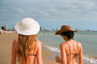 Back view of women standing at beach against sky