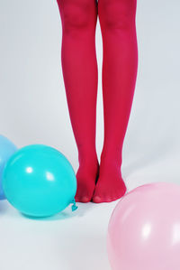 Low section of woman wearing pink stockings standing with balloons against white background