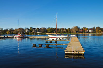 View of sailboats and jetty on river against clear sky