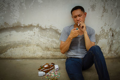 Mature man sitting by narcotics against wall