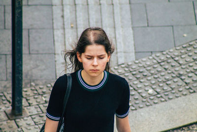 Young woman looking down while standing against brick wall